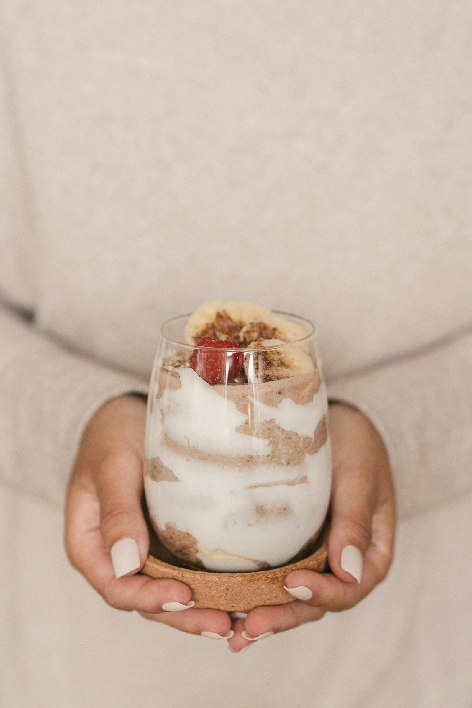 Hands cradling a freshly-made layered shake with banana and raspberry